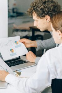 Sales colleagues analyze printed charts next to a laptop.